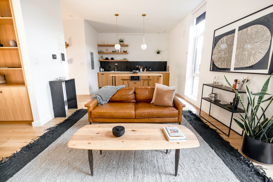 Salon lumineux d'un logement de location courte durée, canapé en cuir cognac et cuisine ouverte