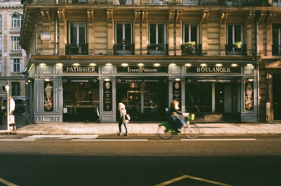Façade d'une boulangerie pâtisserie parisienne au lever du jour, un cycliste passe devant